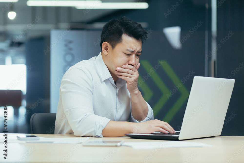 Sick man at work, asian man nauseous poisoned by bad lunch, businessman working in modern office with laptop Sick man at work, asian man nauseous poisoned by bad lunch, businessman working in modern office with laptop