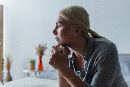 side view of worried blonde woman with menopause looking away in bedroom. photo