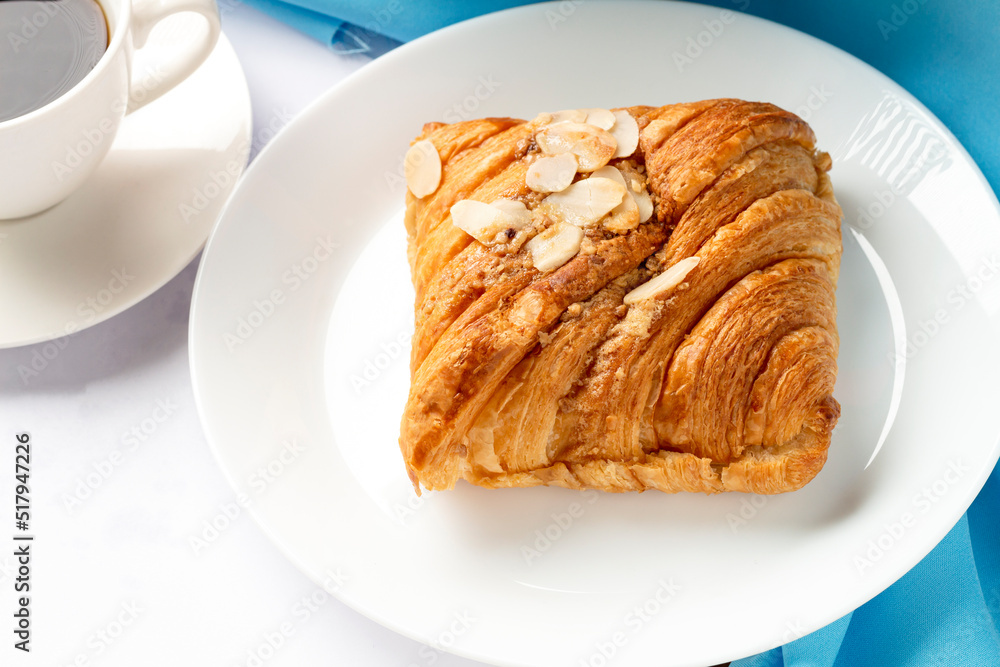 Almond croissant for breakfast on white plate with blue background, flat lay, top view. Almond croissant for breakfast on white plate with blue background, flat lay, top view.