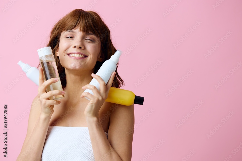 a beautiful, sophisticated red-haired woman stands on a pink background holding four jars of care cosmetics in her hands and smiled broadly. Horizontal photo with empty space