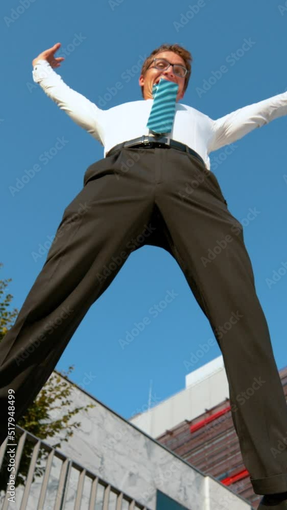 SLOW MOTION, LOW ANGLE: Cheerful businessman jumps and outstretches his arms after a productive day at work. Carefree Caucasian man jumping high in the air as he celebrates finishing a work project. SLOW MOTION, LOW ANGLE: Cheerful businessman jumps and outstretches his arms after a productive day at work. Carefree Caucasian man jumping high in the air as he celebrates finishing a work project.