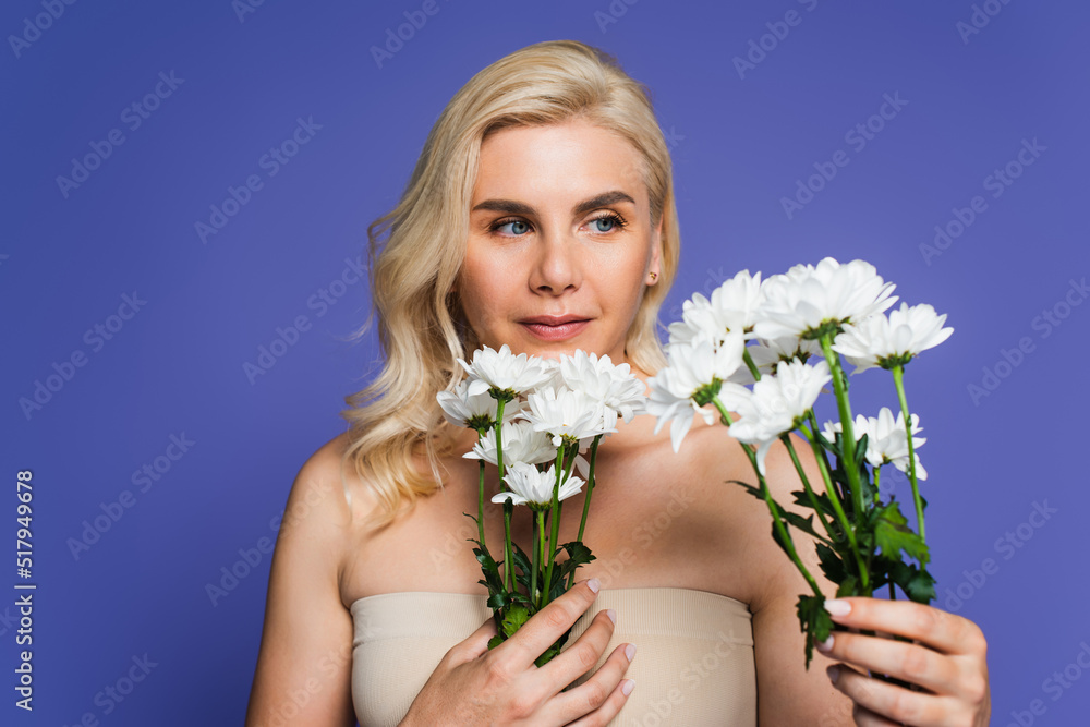 blonde woman with bare shoulders looking at blooming flowers isolated on violet. blonde woman with bare shoulders looking at blooming flowers isolated on violet.