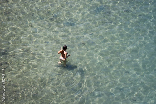 Aerial view to sea and girl in bikini going to swim in transparent water. Woman swimmer, beach vacation in summer