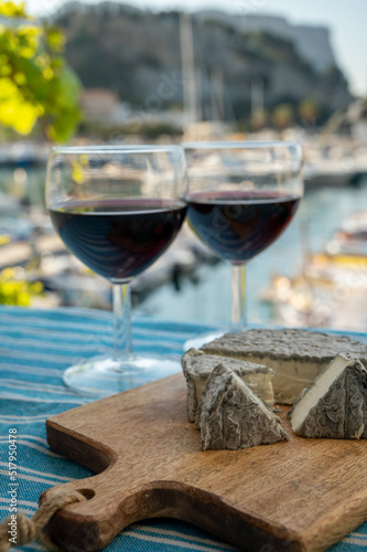 Summer party with red wine and cheeses on outdoor terrace with view on old fisherman's harbour with colourful boats in Cassis, Provence, France
