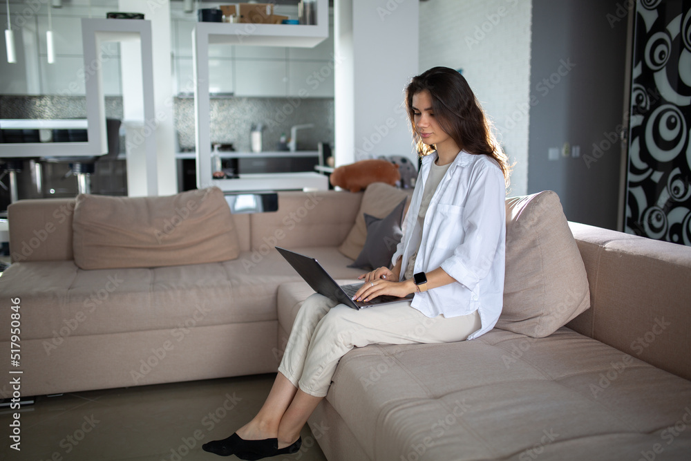 Creative young woman working on laptop in her studio at home on couch Creative young woman working on laptop in her studio at home on couch