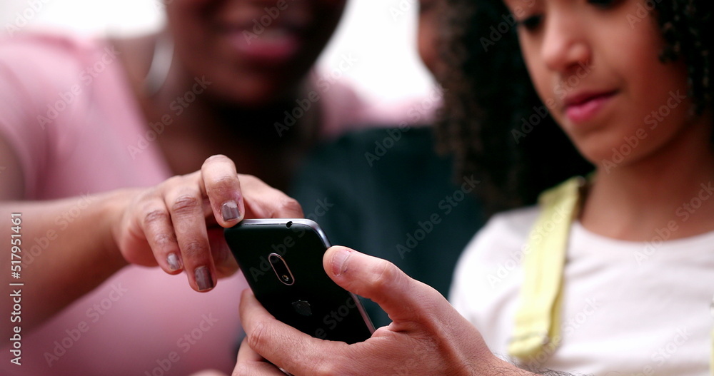 Fototapeta premium Happy multiracial family laughing and smiling together looking at phone. Real life parents and kids laugh and smile