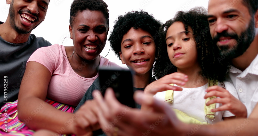 Obraz premium Happy mixed race family looking at phone device laughing and smiling