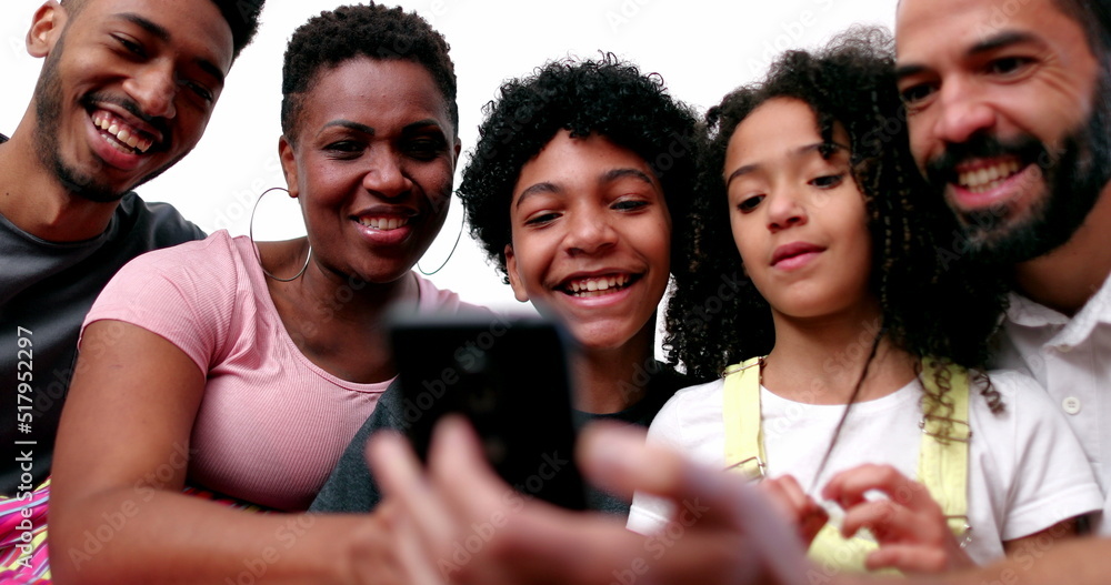 Obraz premium Happy mixed race family looking at phone device laughing and smiling