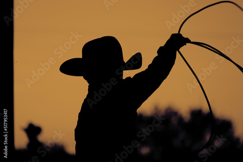 Fényképezés Western rodeo lifestyle shows child cowboy roping practice in silhouette at sunset