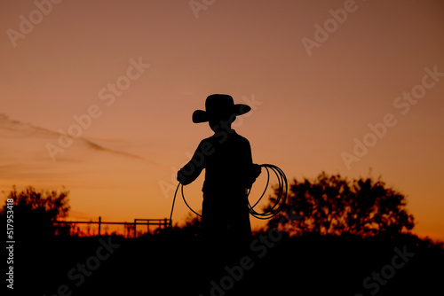 Fotografiet Western industry concept with kid cowboy practicing roping for rodeo at sunset in silhouette on Texas ranch