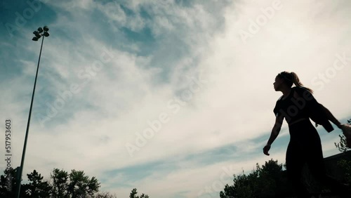 A female softball athlete launches into the sky quickly throwing a caught ball downfield.  Her silhouette passes in front a dramatic sky.  Shot in glorious slow motion. photo