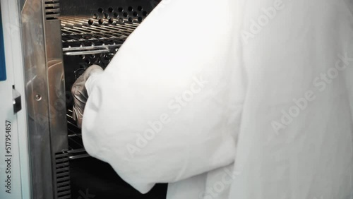 Close-up of nurse in white gloves taking metal pan with clean sterilized surgical tools out of medical autoclave steam sterilizer machine, healthcare worker in hospital operating room, slow motion.