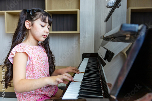 Cute Asian girl is practicing her classical piano lesson at home for song writing and music education concept