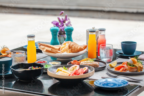 Served breakfast in luxury hotel. Poolside table with various delicious food, freshly squeezed juices, eggs, fruits and smoothie bowl. Morning buffet food in front of swimming pool in modern resort.