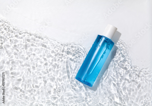 Blue cosmetic bottle on the water surface. Blank label for branding mock-up. Summer water pool fresh concept. Flat lay, top view.	