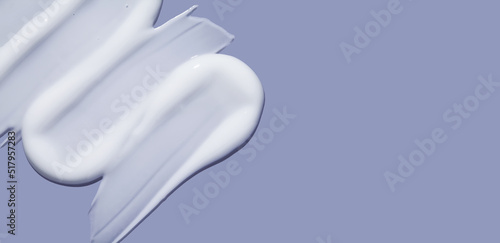 White cosmetic cream lotion swatch smear smudge on violet color background. Skincare hygiene product closeup.