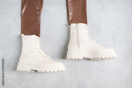 White demi boots made of eco-leather with buckles, laces and brown leather leggings on a gray photo