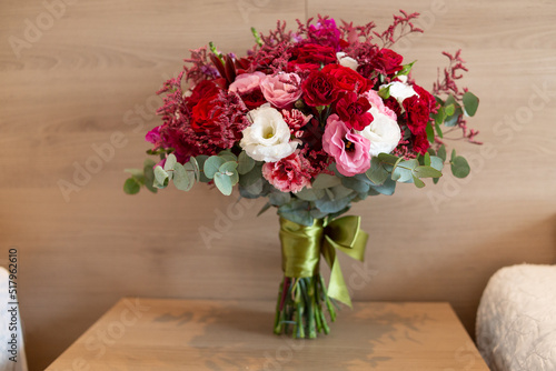Beautiful bouquet of fresh natural flowers, flowers with very vivid colors in white, marsala, red, pink and green. Bouquet on top of a wooden table and wooden wall behind. Full front view.