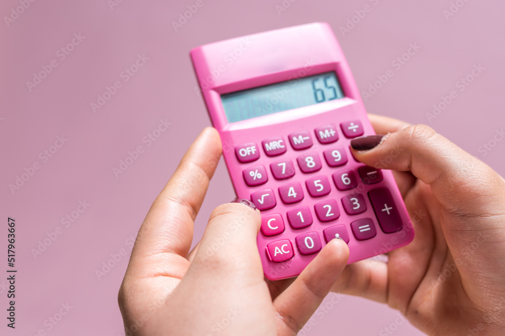 Hands using a pink calculator with white numbers on a pink surface Hands using a pink calculator with white numbers on a pink surface