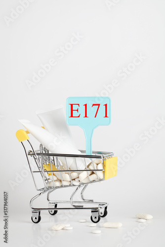 Titanium dioxide, E171, dangerous additive concept. gum, pills, toothpaste, cream in basket and sign with E171 on white background. copy space photo