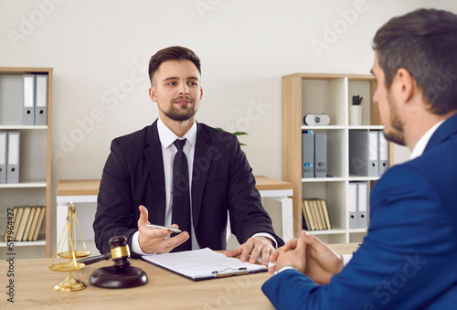 Lawyer having a meeting with a new client. Young male attorney in suit and tie sitting at office desk, sharing legal advice, explaining inheritance process, trying to help. Law consultation concept photo