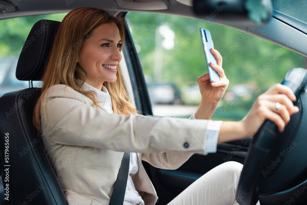 Beautiful business woman using mobile phone in car. Business woman driving car and using phone for video call.