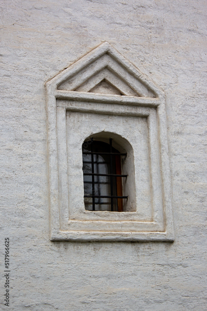 Arched window closed with black iron bars on a old white stucco wall of the monastery. Close-up of Medieval cast-iron shutters on the facade of an old building