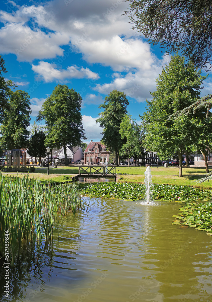 Beautiful idyllic green dutch town park, pond, wood bridge, blue summer sky fluffy clouds - Nuenen, Netherlands