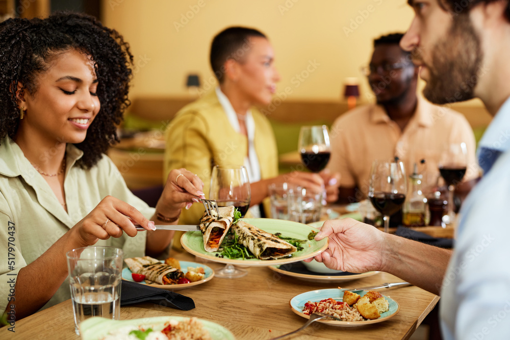 A happy multicultural couple sits in a restaurant with their friends and eats dinner.