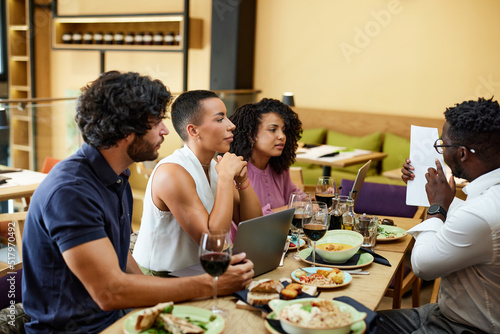 A group of casual businesspeople is sitting in a restaurant for a meeting, discussing a project while having dinner.