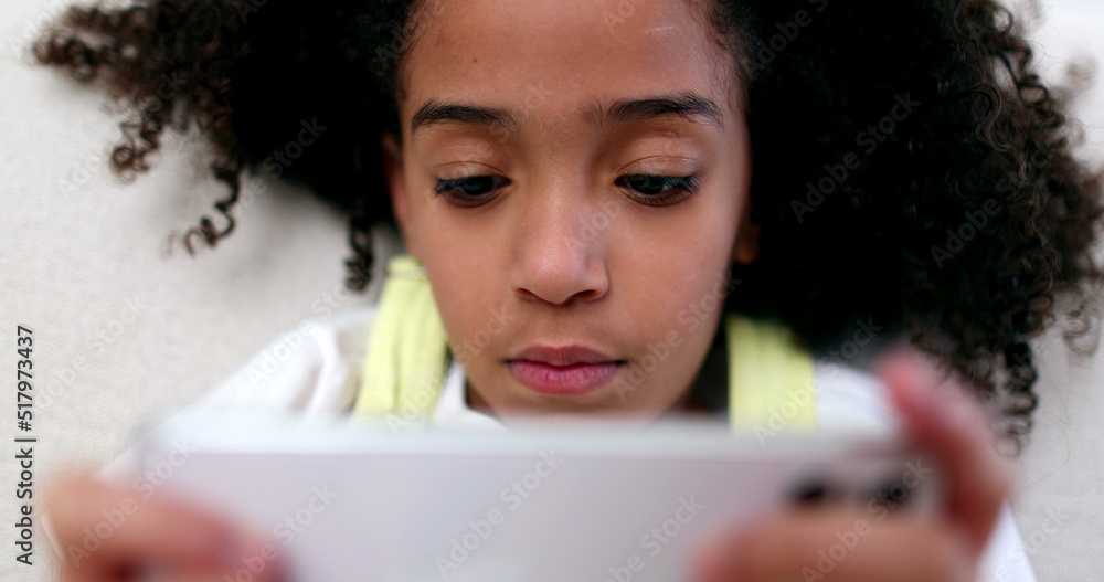 Little girl holding smartphone. Mixed race black child watching content on phone Little girl holding smartphone. Mixed race black child watching content on phone