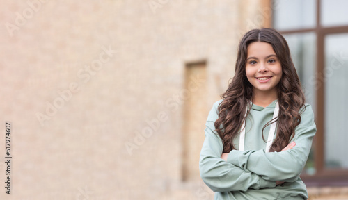 Confident teenage girl happy smiling in casual hoodie keeping arms crossed blurry outdoors, copy space
