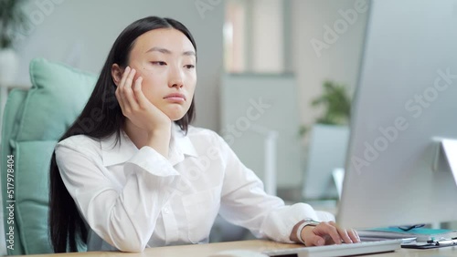 Bored sleepy Asian office worker sitting at work workplace at computer desk leaning on hand. Tired woman. Exhausted young Businesswoman employee. Portrait Depressed, unhappy, workless female manager photo