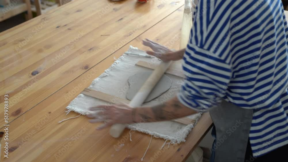 Female ceramist using a rolling pin to roll out slab of clay while working in workshop, creating handcrafted items to sell. Pottery student learning basic hand building techniques in ceramics school Female ceramist using a rolling pin to roll out slab of clay while working in workshop, creating handcrafted items to sell. Pottery student learning basic hand building techniques in ceramics school