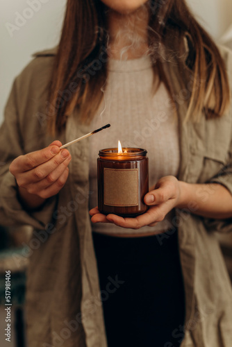 a burning candle in a jar close-up in the hands of a young beautiful woman. the girl lit a candle in her hands.