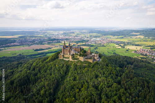 Drone shot of Hohenzollern Castle on forested mountain top in the Swabian Alps in summer. Scenic aerial view of old German Burg. Famous fairytale Gothic landmark in Stuttgart vicinity
