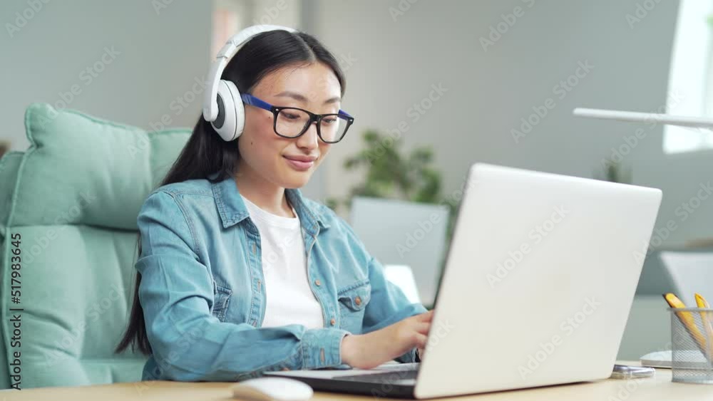 stylish trendy young asian woman working on laptop computer listen music sounds or radio in headphones in modern office. Pleasant Girl student worker employee enjoying at workplace or home indoors stylish trendy young asian woman working on laptop computer listen music sounds or radio in headphones in modern office. Pleasant Girl student worker employee enjoying at workplace or home indoors