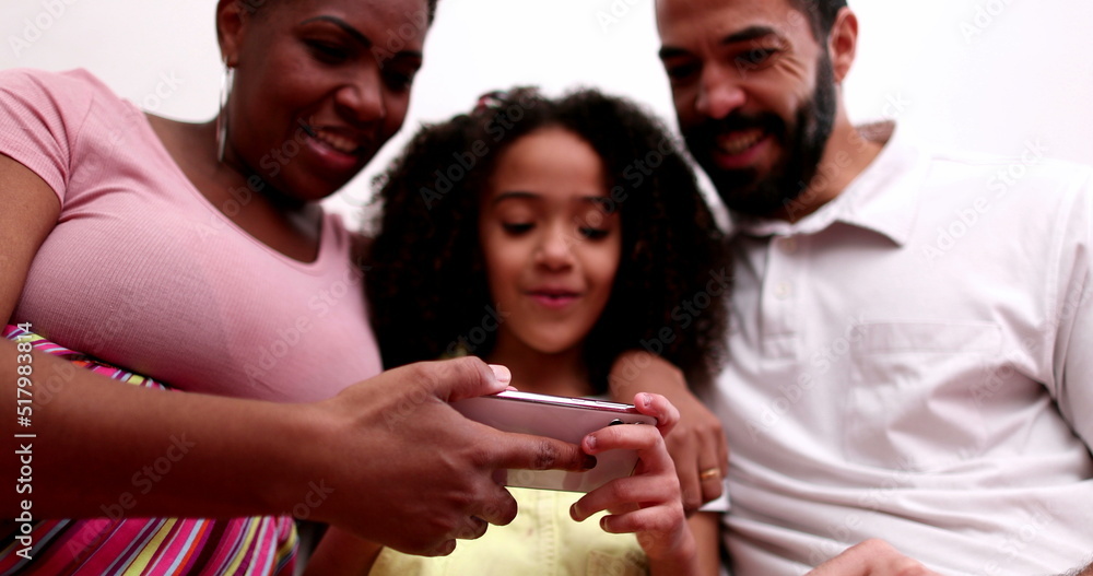 Fototapeta premium Mixed race couple and child holding smartphone. Father pointing to screen laughing and smiling