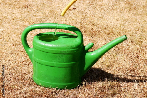 Canvas Print Drought effected grass with green watering can being filled with a hose