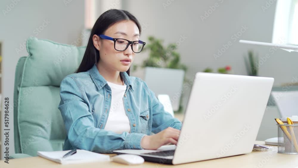 young stylish beautiful asian woman in glasses and casual clothes working on laptop computer in modern office. worker is sitting at desk in workplace. employee uses a PC browsing, texting. Asia young stylish beautiful asian woman in glasses and casual clothes working on laptop computer in modern office. worker is sitting at desk in workplace. employee uses a PC browsing, texting. Asia