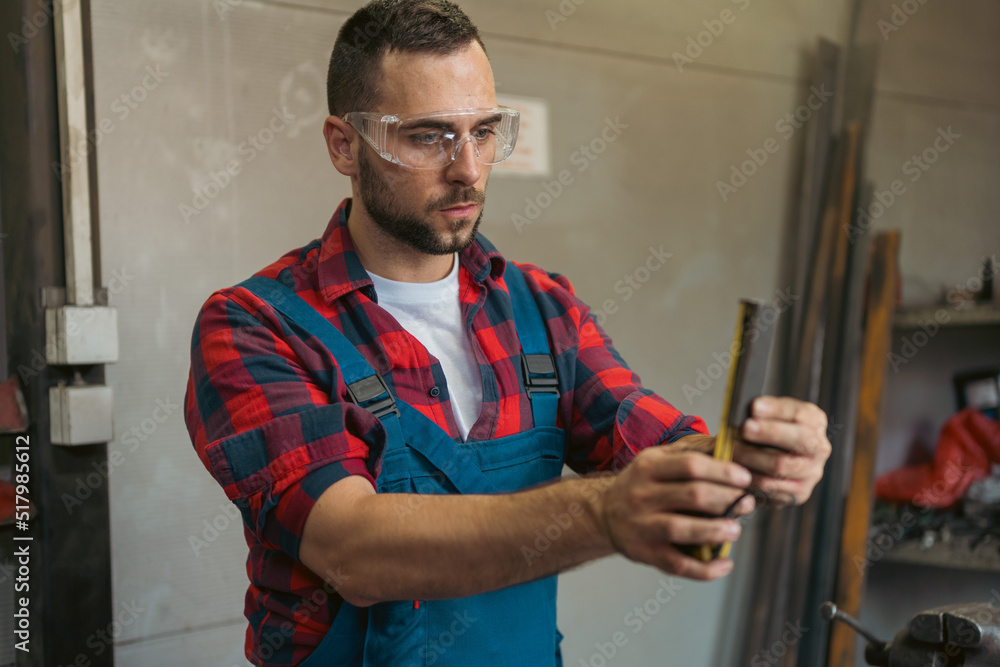Young male mechanic being focused on measuring out elements for machine at his work space Young male mechanic being focused on measuring out elements for machine at his work space