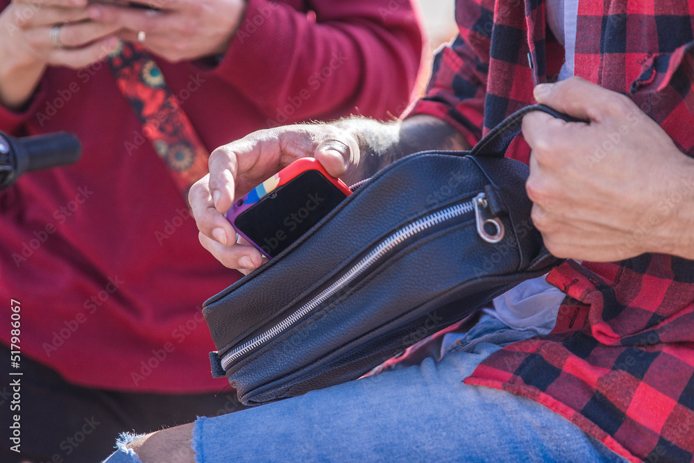 Close up of Latin gay taking out a mobile phone from a leather case outdoors. LGBTQ concept.