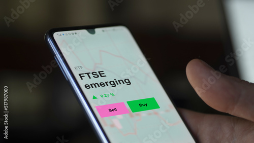 An investor's analizing the ftse emerging etf fund on a screen. A phone shows the prices of FTSE emerging