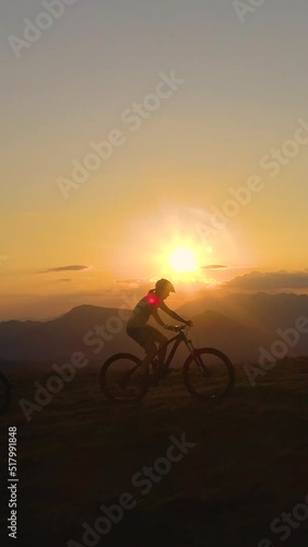 Wallpaper Mural AERIAL, SILHOUETTE, LENS FLARE: Breathtaking evening sunbeams shine on the tourists riding ebikes in the scenic nature. Three downhill bikers pedalling their bicycles up along grassy hill at sunrise. Torontodigital.ca