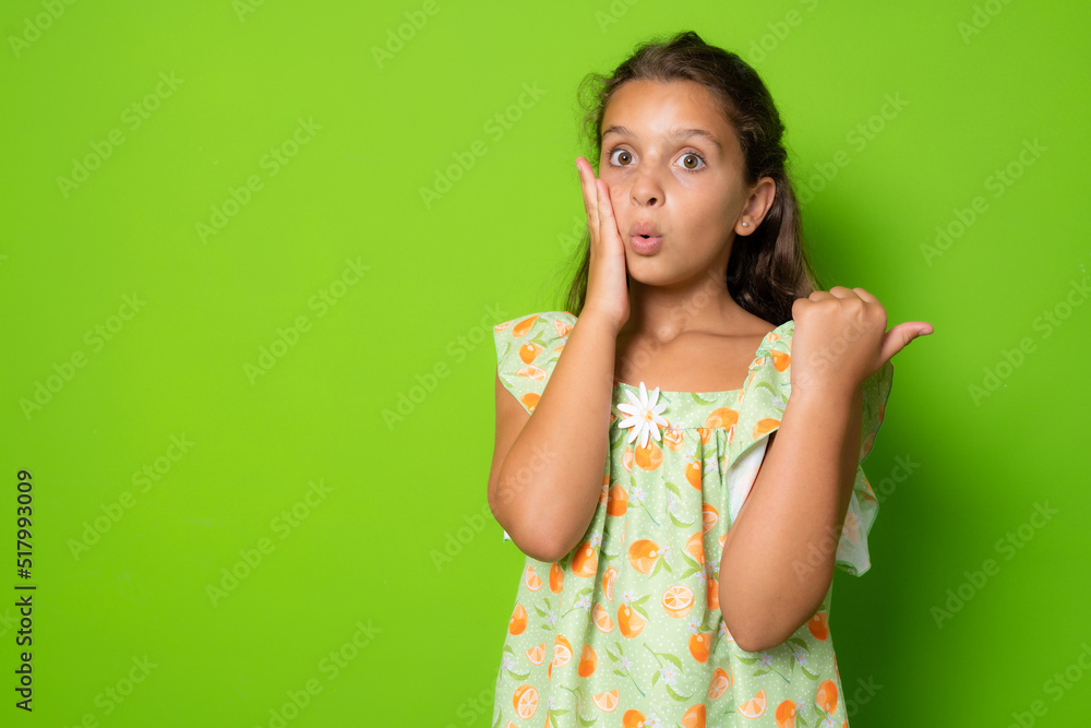 Shocked amazed cute brunette little girl kid, touch face stunned, turn pointing right copy space amazed, drop jaw wondered, stare speechless and astonished awesome promo, stand green background amused Shocked amazed cute brunette little girl kid, touch face stunned, turn pointing right copy space amazed, drop jaw wondered, stare speechless and astonished awesome promo, stand green background amused