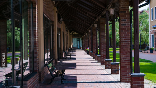 Alley with benches and columns from the side. Sunny day. Boutique shops. Manufactory. Not destroyed. Empty street.