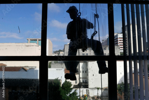 Rappeling man work on external window cleaning service and building repair. Silhouette workman rappel renovating building. Carpenter construction worker