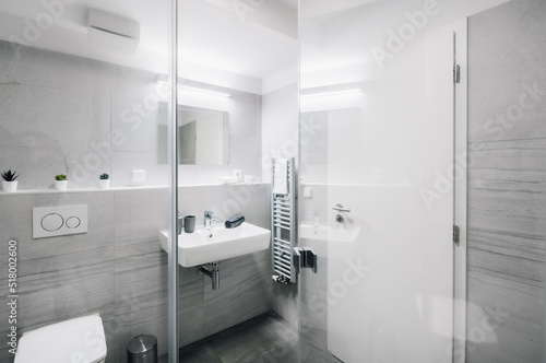 A small modern bathroom with a large mirror  square sink  toilet and glass shower enclosure. There are also some additional items as towel  candles  soap dispenser  waste bin  etc.