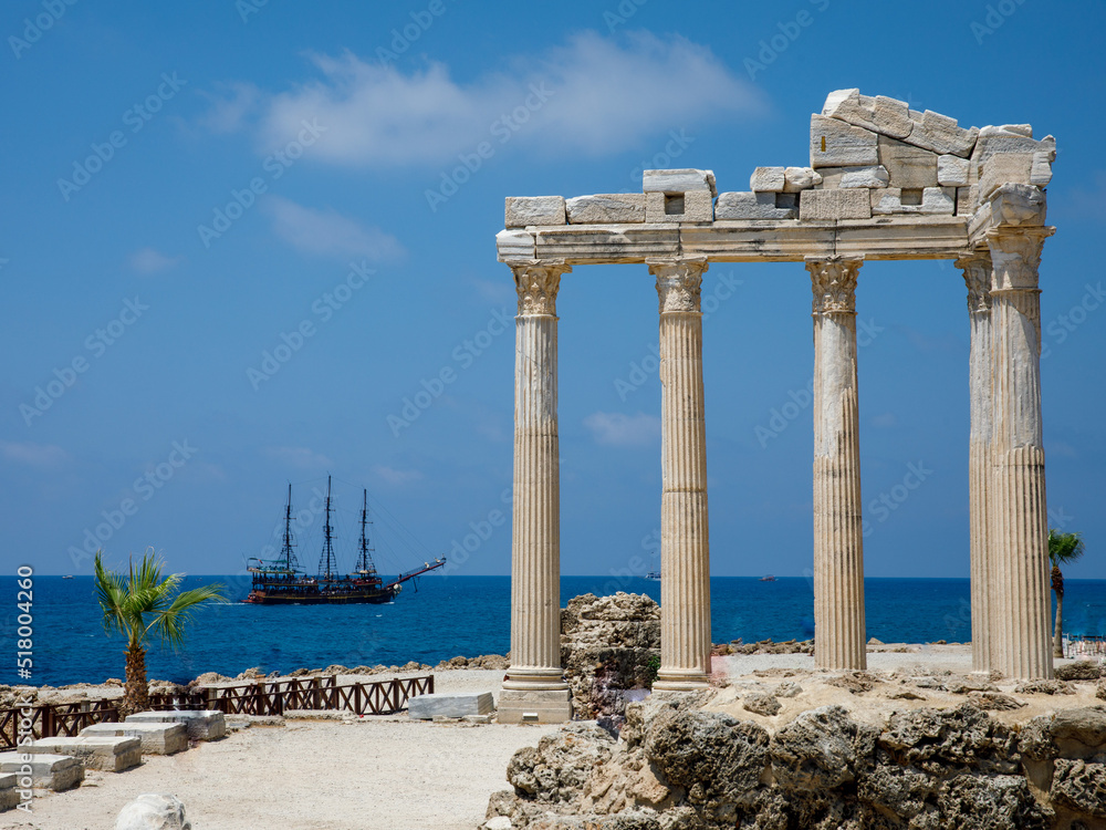 Ruins of the Temple of Apollo with pirate ship in old town of Side at beautiful summer day, Antalya, Turkey