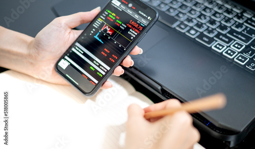Female trader investor broker analyst holding a smartphone in hand analyzing stock market trading charts indexes data checking price using mobile